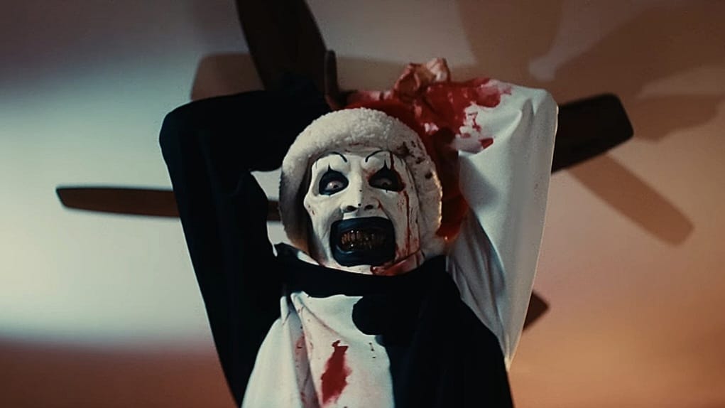 David Howard Thornton as Art the Clown gives a huge sinister smile as he raises an axe over his head getting ready to swing it down in Damien Leone's TERRIFIER 3. 