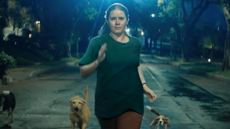 Amy Adams runs down the middle of an empty street next to a bunch of dogs at night in the dark absurdist comedy NIGHTBITCH.