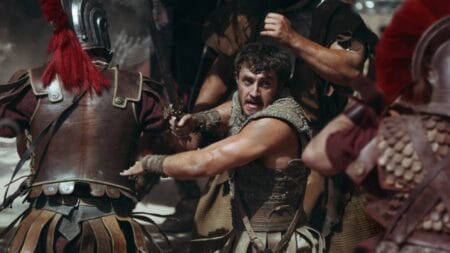 Paul Mescal stars as Lucius Verus swinging his sword in the middle of a huge epic battle with Roman soldiers in the legacy sequel GLADIATOR II directed by Ridley Scott.