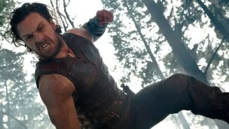Aaron Taylor-Johnson raises his fist for a powerful punch in full costume as Kraven the Hunter from the 2024 Sony Marvel movie.