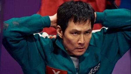 ‘Squid Game’ Season 2 Review – A Shocking and Unpredictable, Yet Slightly Fustrating Continuation Seong Gi-hun, played by Lee Jung-jae, kneels down with his hands on his head as guards dressed in pink surround him during the middle of the squid game competition in SQUID GAMES Season 2 streaming only on Netflix.