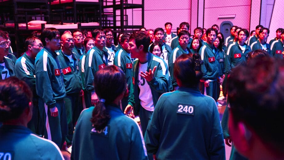 Lee Jung-jae as Seong Gi-hun gives an empowering speech at the center of a large crowd of contestants wearing green tracksuits in SQUID GAME Season 2 on Netflix. 