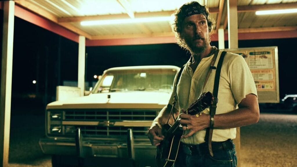 Actor Matthew McConaughey stars as rural Oklahoma honey trader Amziah King posing in a fast food parking lot with a banjo guitar in the new crime thriller movie THE RIVALS OF AMZIAH KING.