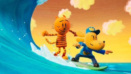 The villainous orange cat Petey and the hybrid police officer superhero Dog Man surf on a vibrant blue wave together in the animated DreamWorks film DOG MAN, which is included in the Peacock May 2025 list of new movies and TV shows.