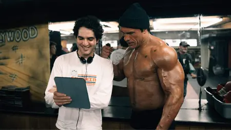 Director Benny Safdie and actor Dwayne Johnson in character as iconic MMA fighter Mark Kerr look at a script together on the training gym set of their sports biopic THE SMASHING MACHINE.