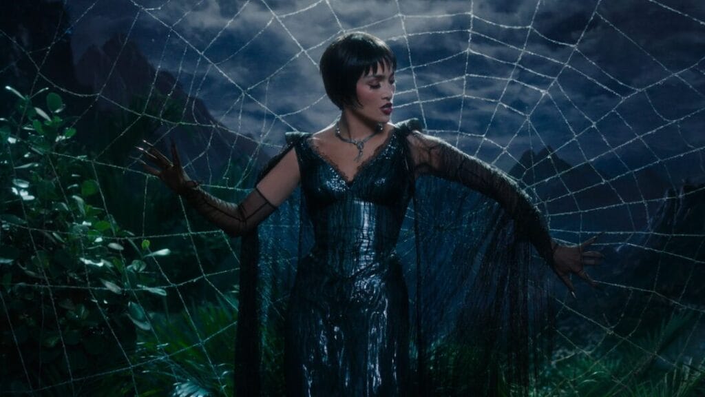 Jennifer Lopez stars as the titular Spider Woman wearing a lavish black dress as she strikes a dramatic pose with her arms open against a giant spider web behind her in the KISS OF THE SPIDER WOMAN movie musical.