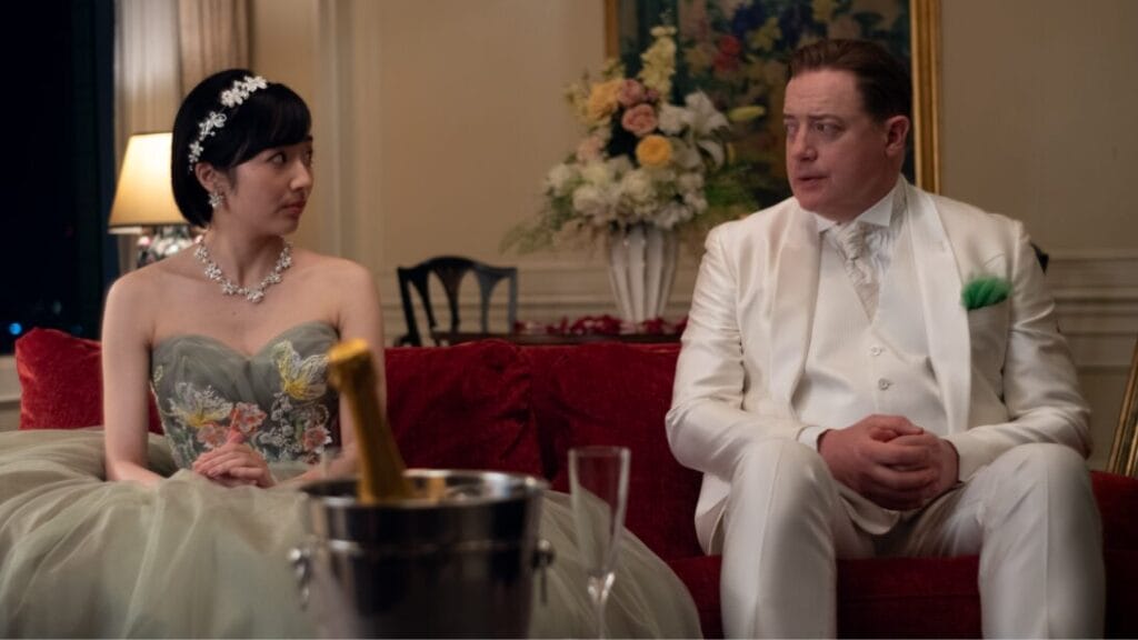 Brendan Fraser and Misato Morita awkwardly sit and stare across from each other as pretend groom and bride while wearing an all-white tuxedo and beautiful green wedding dress in the dramatic comedy movie RENTAL FAMILY.