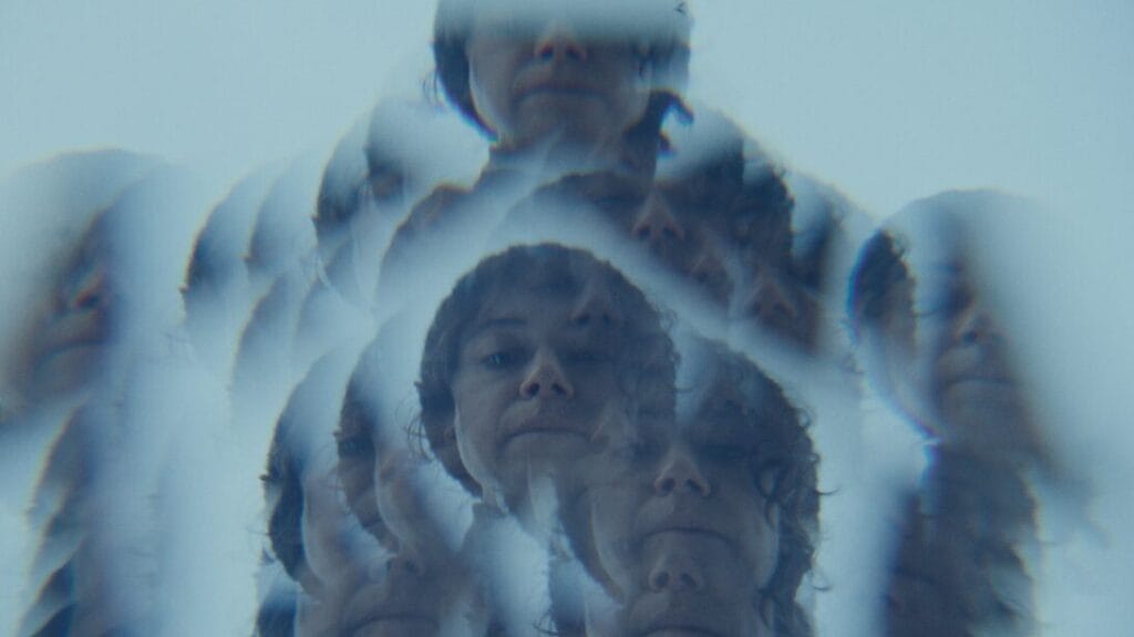 A kaleidoscopic image of Tatiana Maslany's face looking down at a river in total hypnosis from the horror film KEEPER.