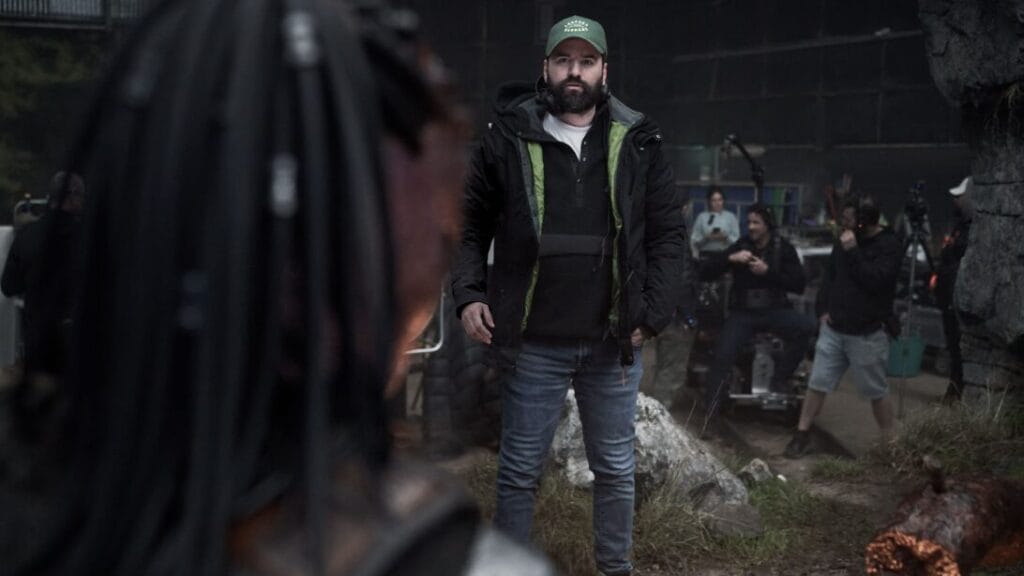 Director Dan Trachtenberg examines an actor wearing a full body Yautja warrior costume on the jungle set of the movie PREDATOR: BADLANDS.