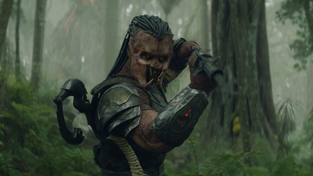 The young runt Yautja warrior Dek raises his large metallic spear as he steps into the jungles of the alien death planet Genna for the first time in the film PREDATOR: BADLANDS. 