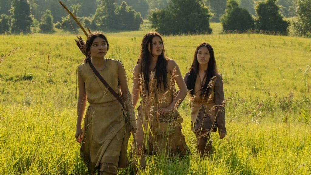 Three female members of the fictional Shokopiwah Native American tribe cross a large beautiful field in a historical flashback segment from episode 4 of IT: WELCOME TO DERRY.