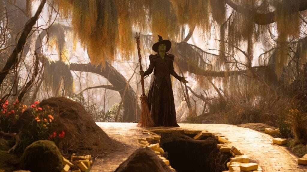 Cynthia Erivo as Elphaba Thropp, in her updated Wicked Witch of the West black costume, belts out a song in the middle of a beautiful forest with old brown trees in the movie musical sequel WICKED: FOR GOOD.
