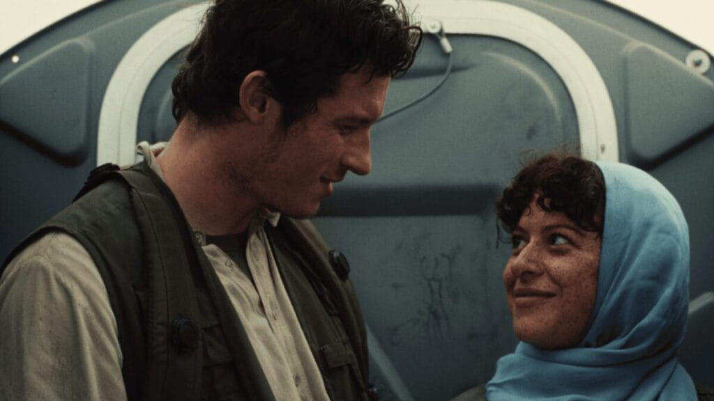 Callum Turner and Alia Shawkat meet in secrecy inside a rundown porta-potty while dressed as Middle Eastern civilians in the war satire ATROPIA.