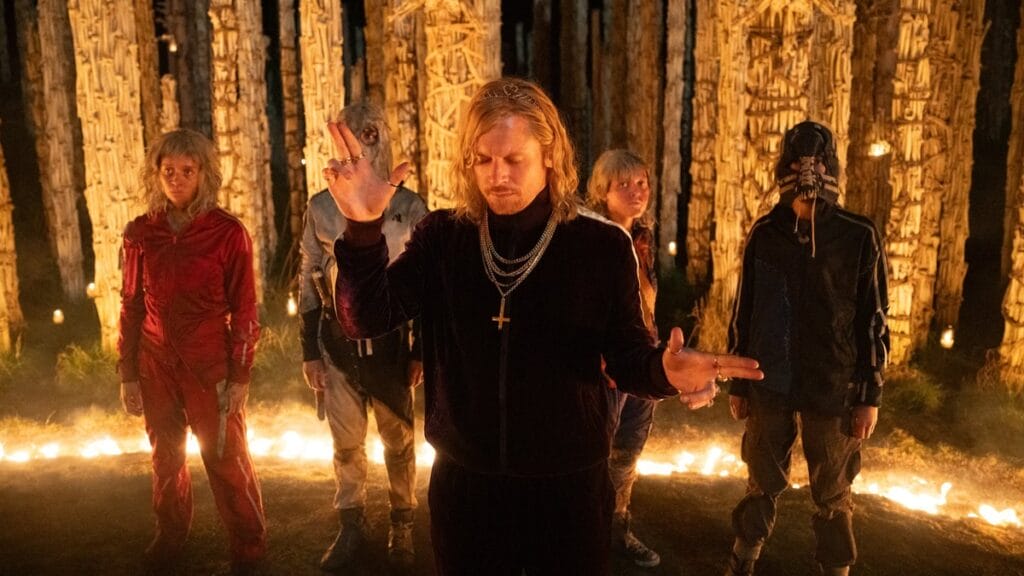 Jack O'Connell stars as the cult leader Sir Lord Jimmy Crystal striking a rock star like pose as his devoted followers stand behind him at the center of a bunch of tall pillars made of human skulls in the sequel 28 YEARS LATER: THE BONE TEMPLE.