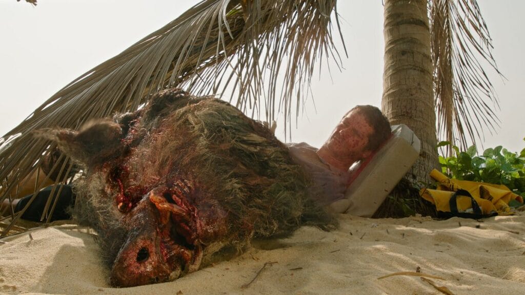 The bloody decapitated head of a large boar sits in front of Dylan O'Brien's shocked face in the horror thriller film SEND HELP.