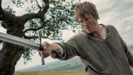 Peter Claffey stars as Ser Duncan the Tall raising his large and shiny sword towards the camera in an epic battle shot from the Game of Thrones spin-off show A KNIGHT OF THE SEVEN KINGDOMS.