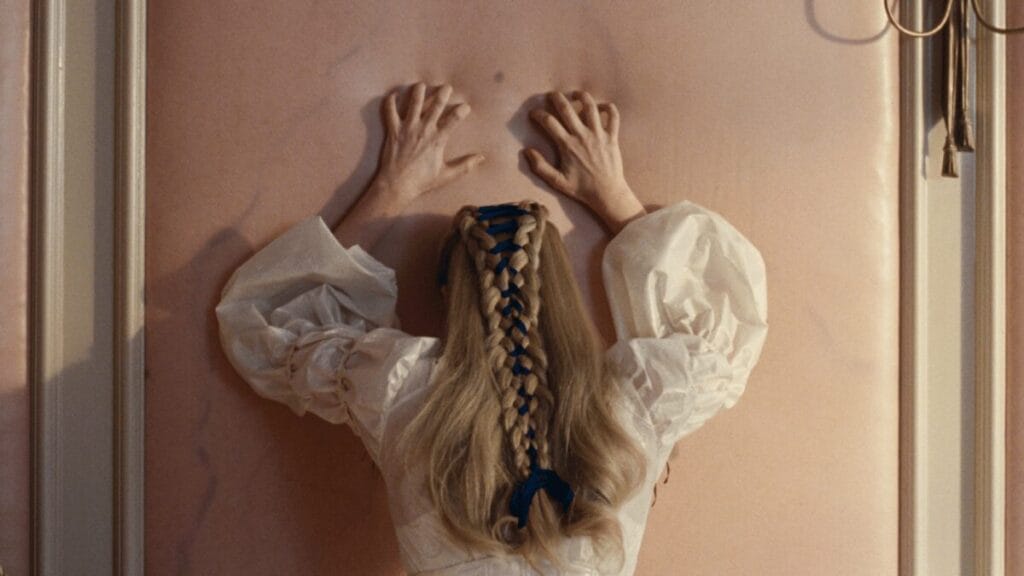 Margot Robbie throws her arms and hands up against a pink wall in total distress in Emerald Fennell's WUTHERING HEIGHTS film adaptation.