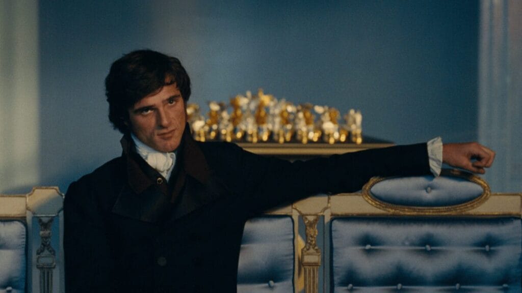 Jacob Elordi stars as Heathcliff sitting down in a luxurious couch while wearing 18th-century classic attire in Emerald Fennell's film adaptation of WUTHERING HEIGHTS.