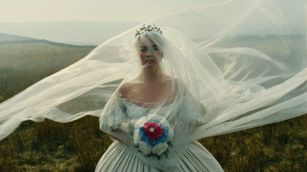 Margot Robbie stars as Cathy Earnshaw wearing a large beautiful white wedding dress while standing on a lavish hillside in Emerald Fennell's movie adaptation of WUTHERING HEIGHTS.