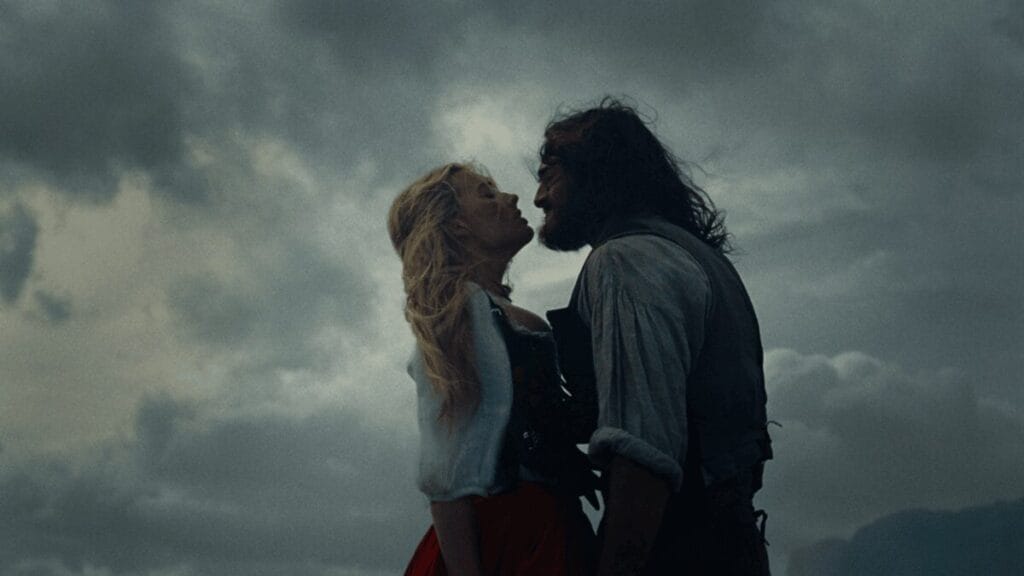 Margot Robbie and Jacob Elordi embrace each other romantically against a moody backdrop of dark stormy clouds in Emerald Fennell's WUTHERING HEIGHTS movie adaptation. 