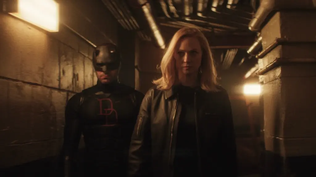 Daredevil wearing his new black suit walks alongside Karen Page down a dimly-lit industrial hallway in DAREDEVIL: BORN AGAIN Season 2.