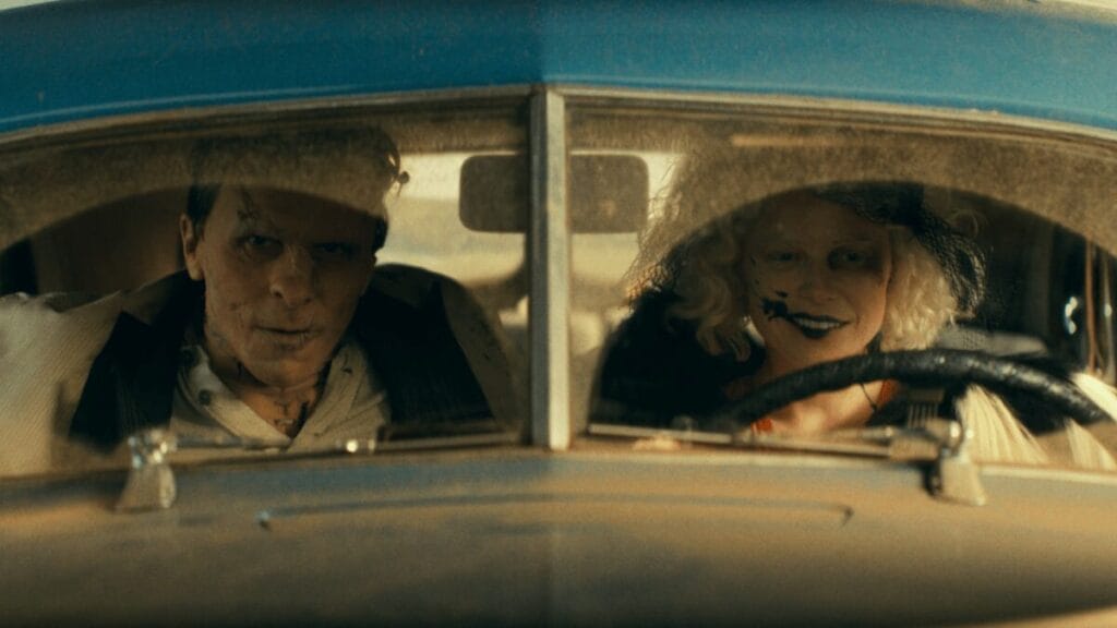 Christian Bale as Frankenstein's Monster and Jessie Buckley as The Bride drive away in a 1930s getaway car in Maggie Gyllenhaal's THE BRIDE!