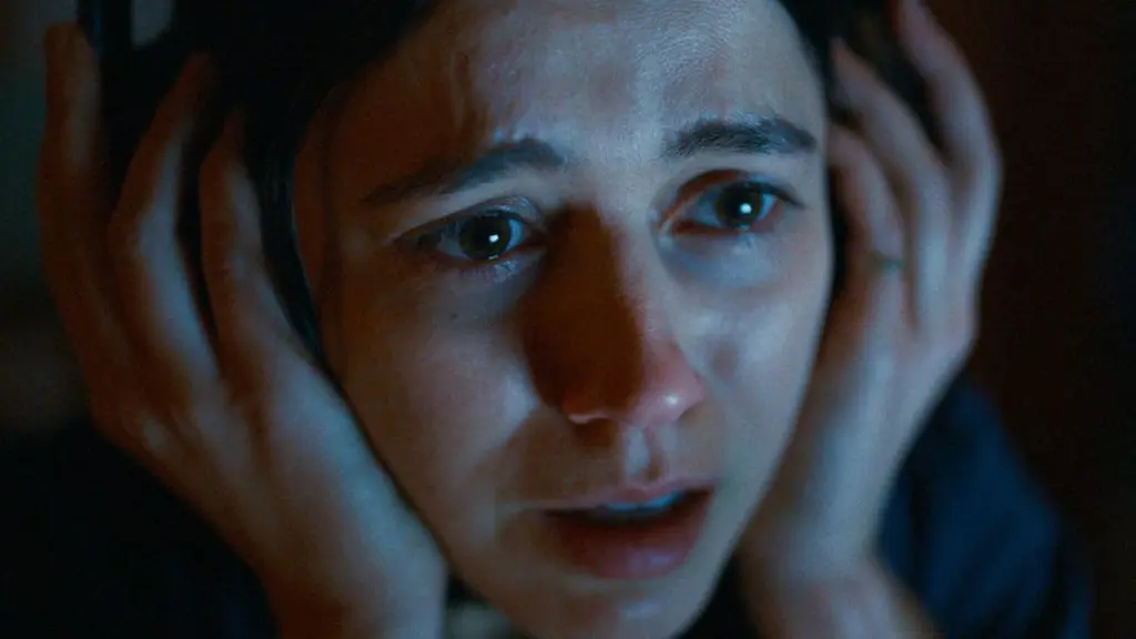 A close-up shot of Nina Kiri's face looking incredibly scared as she holds her headphones tight with fear from the A24 horror movie UNDERTONE.