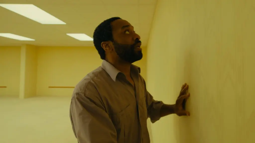 Chiwetel Ejiofor looks terrified as he presses his hands against a yellow wall and tries to escape the barren dimension of the Backrooms in the A24 movie.