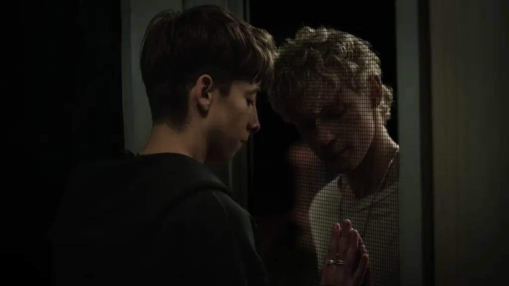 ‘Leviticus’ Review – Desire is Deadly in This Queer Australian Horror Film Joe Bird and Stacy Clausen try to embrace each other and press each other's hands through a screen door in the queer horror movie LEVITICUS.