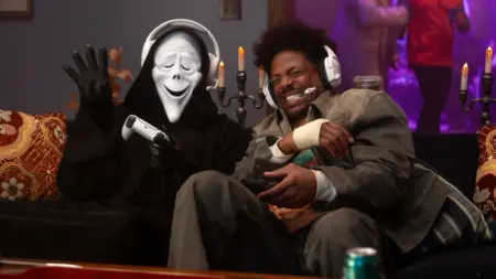 Ghostface making a funny face while sticking his tongue out plays video games with Shorty played by Marlon Wayans in SCARY MOVIE 6.