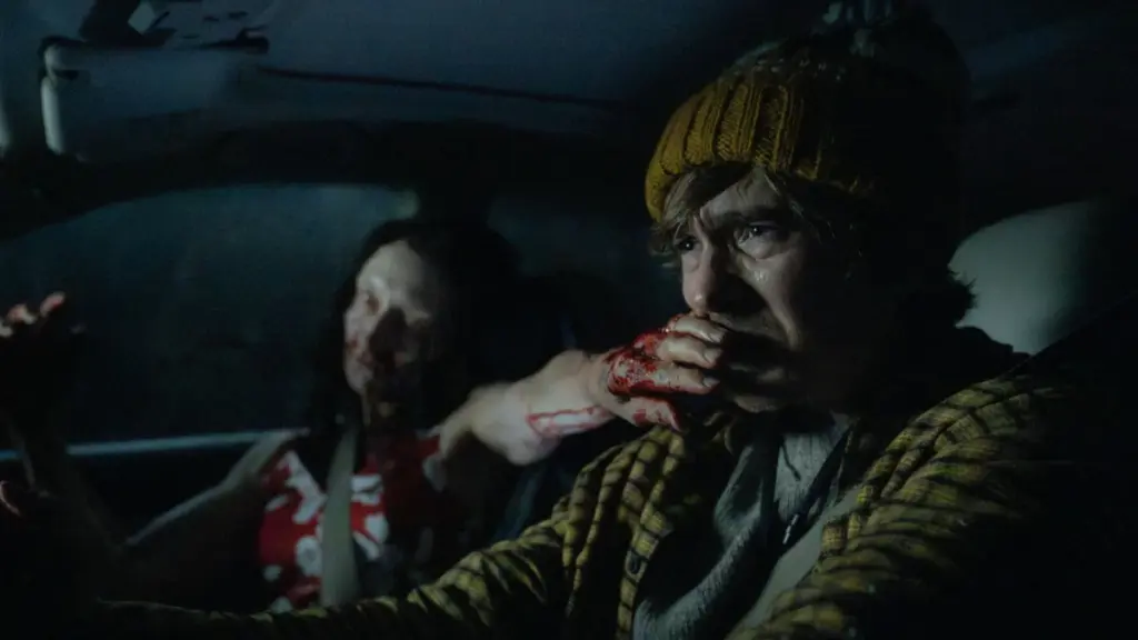Austin Abrams makes a disgusted face as a female zombie puts its hand over his mouth while he tries to safely drive a car in Zach Cregger's RESIDENT EVIL.