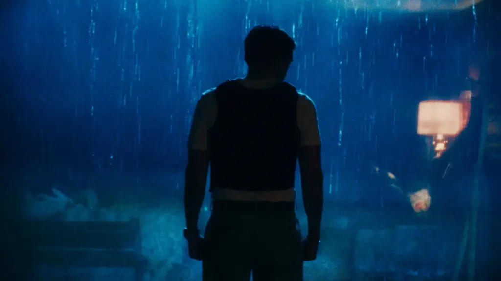 A dark and ominous silhouette of Robert Pattinson as To Catch a Predator host Chris Hansen standing in front of a large window with heavy rain outside in Lance Oppenheim's PRIMETIME. 