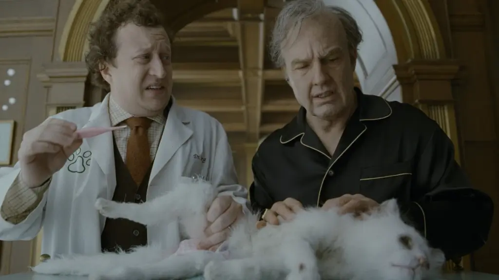 Dr. Berg, played by Ross Hatt, and Digger Rockwell, played by Tom Cruise, inspect his old white cat named Maggie, which hilariously looks like a flimsy puppet, in DIGGER.