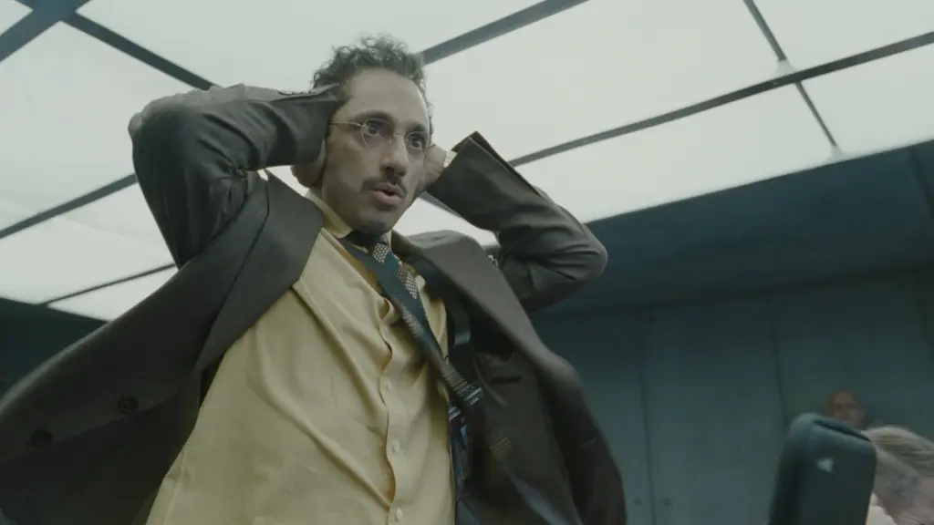 Riz Ahmed stars as Dr. Ganesh, one of Digger Rockwell's scientists, holding a funny pose as he covers his ears with his hands in DIGGER.