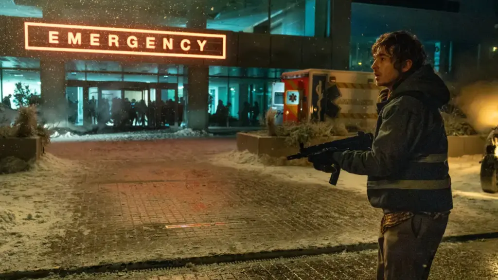Austin Abrams stands outside of a Raccoon City General Hospital in the snow in Zach Cregger's RESIDENT EVIL. 