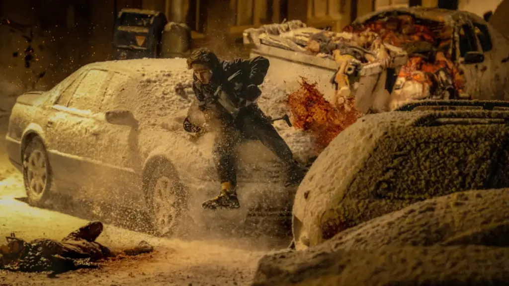 Austin Abrams runs for his life across a snowy street in Raccoon City while being chased by zombies in RESIDENT EVIL.  