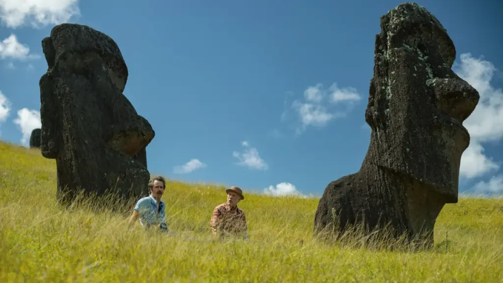 Sam Rockwell and John Malkovich sit together in a large green field next to the Eastern Island heads in Martin McDonagh's WILD HORSE NINE.