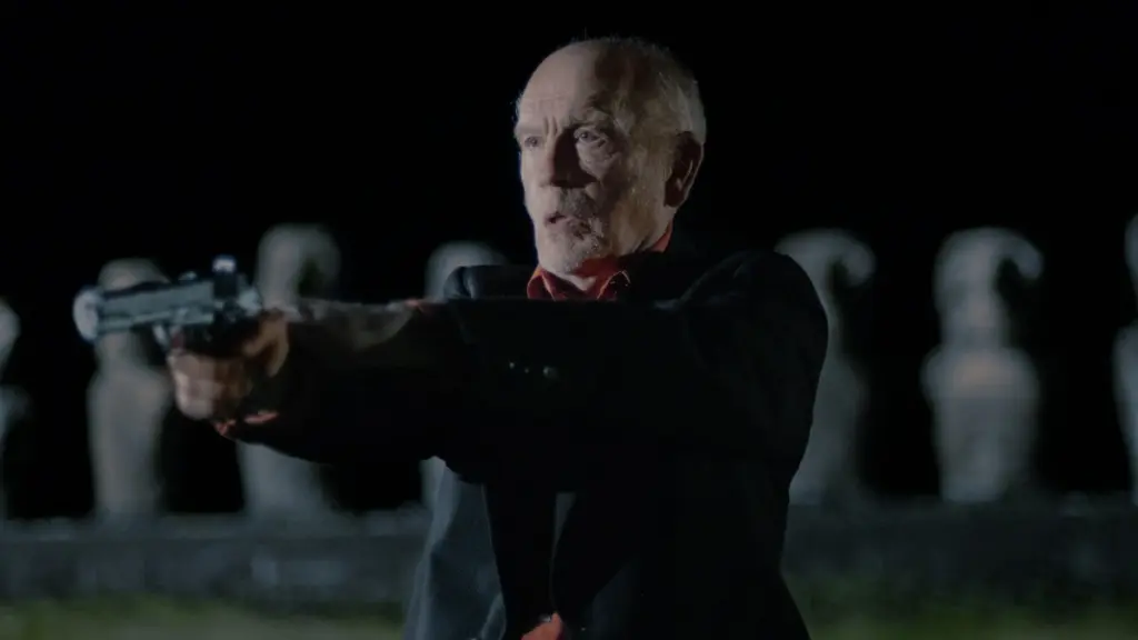 John Malkovich stars as veteran CIA officer Chris shooting a gun on Eastern Island in the action-thriller WILD HORSE NINE directed by Martin McDonagh.