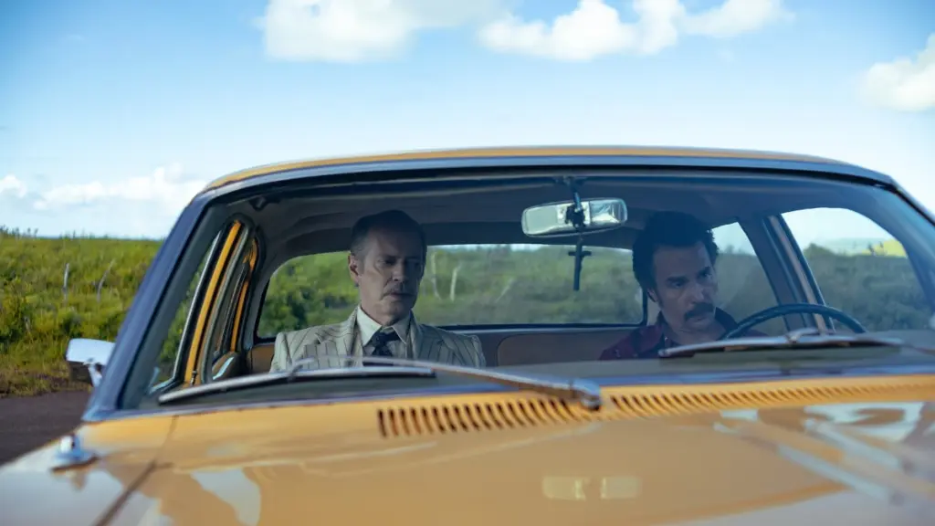 Steve Buscemi and Sam Rockwell sit together in a bright yellow car on Eastern Island in black comedy action-thriller WILD HORSE NINE.