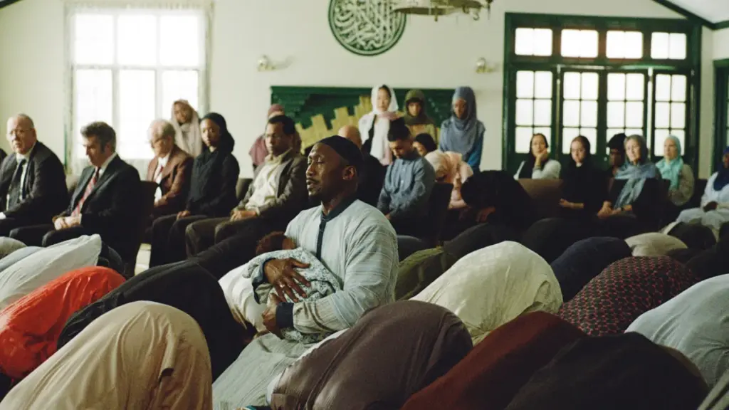 Mahershala Ali prays inside a packed mosque while holding his baby child passionately in YOUR MOTHER YOUR MOTHER YOUR MOTHER.