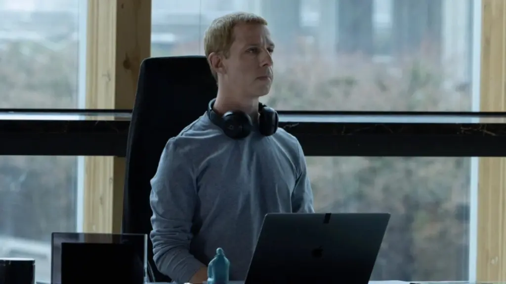 Jeremy Strong stars as billionaire Facebook CEO Mark Zuckerberg sitting at his desk with headphones around his neck in THE SOCIAL RECKONING.