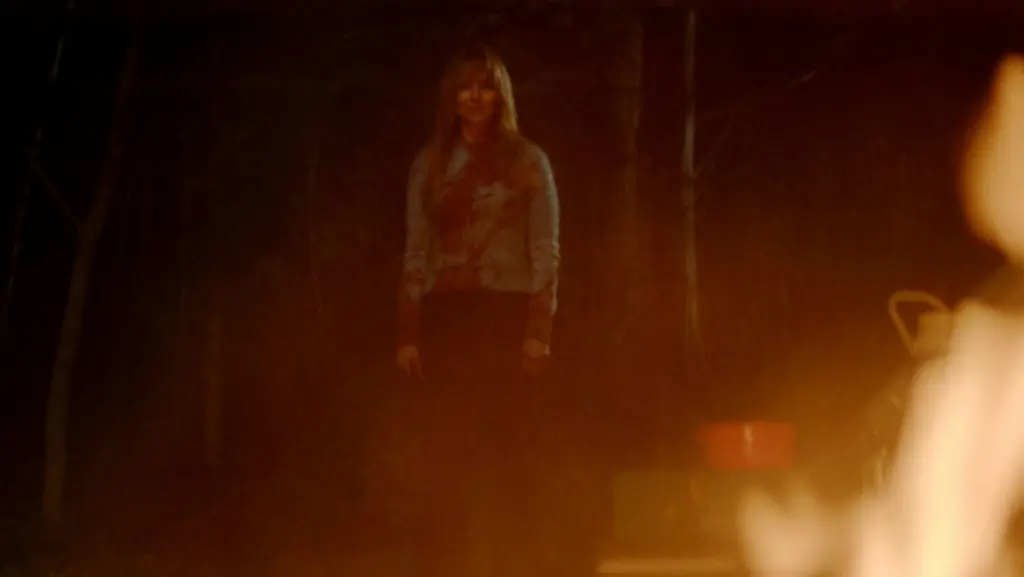 Linda Cardellini stars as the female killer Pamela Voorhees standing in front of an ominous camp fire in the Friday the 13th prequel series CRYSTAL LAKE on Peacock. 